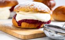 Fastelavnsboller med krem og syltetøy på en skjærefjøl, med flere boller i bakgrunnen.