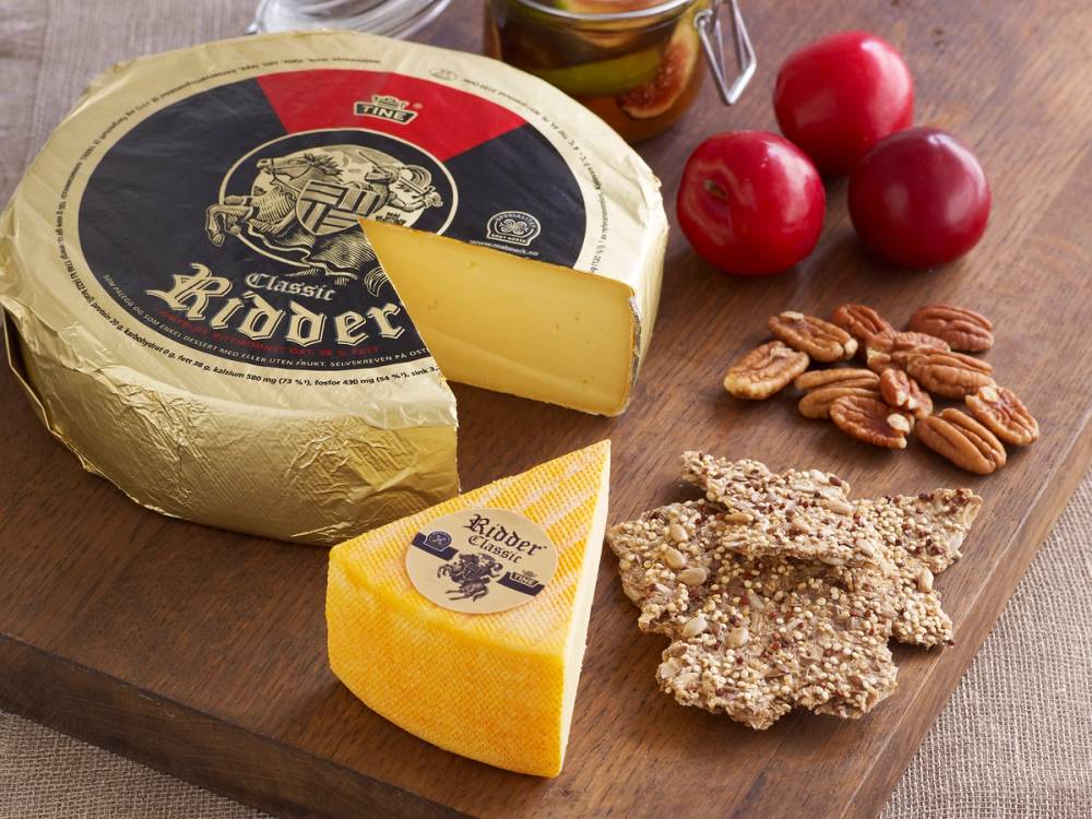 Ulike typer ost, nøtter, epler og kjeks på et trefat, med en hel og en skåret ost i fokus.