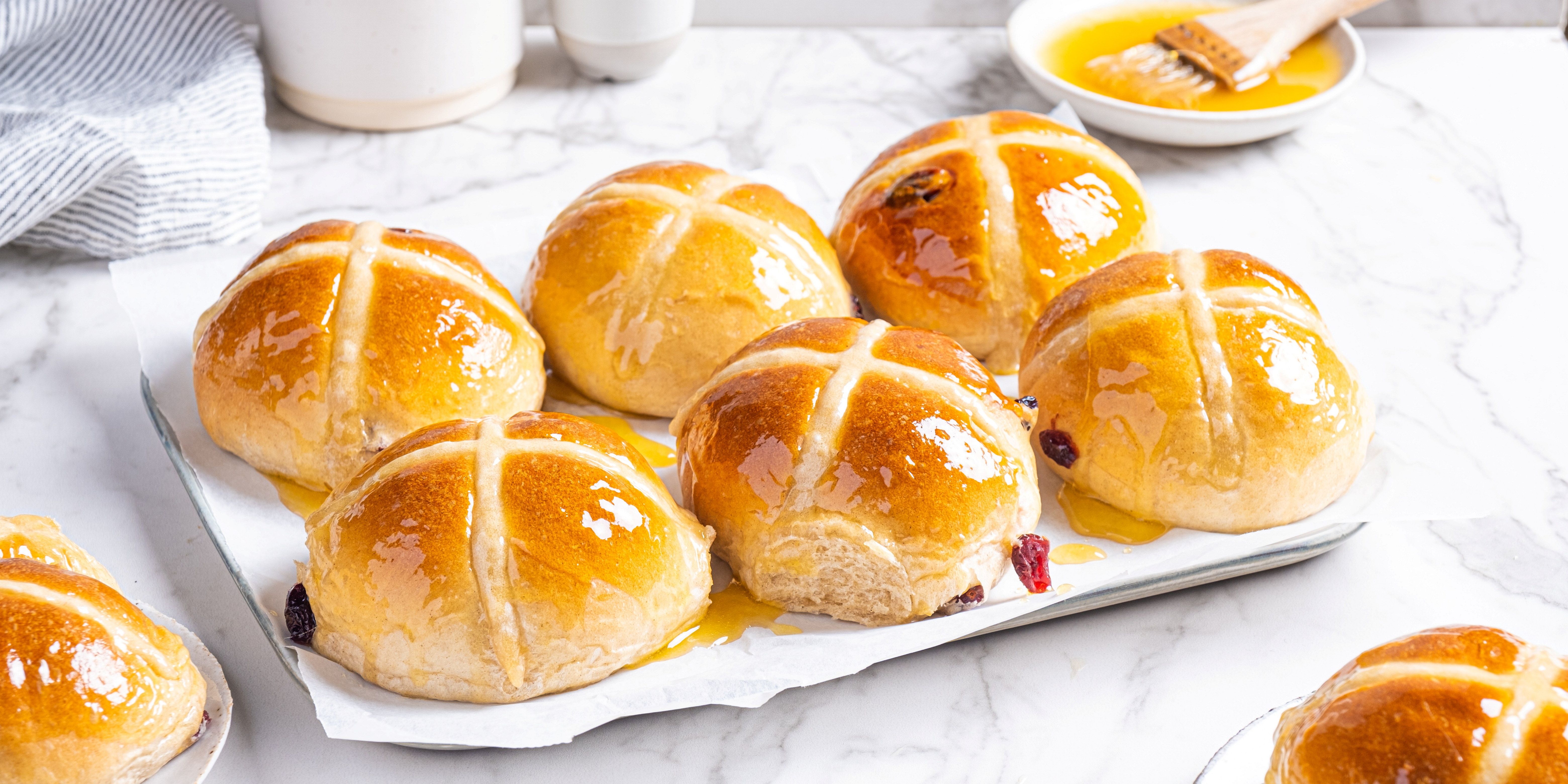 Syv varme hot cross buns med kryss på toppen ligger på et hvitt serveringsfat.