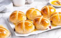 Syv varme hot cross buns med kryss på toppen ligger på et hvitt serveringsfat.
