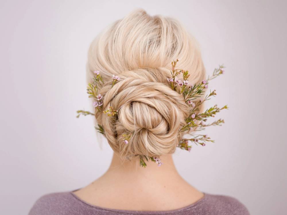 En person med lyst, oppsatt hår dekorert med små blomster og grener sett bakfra.