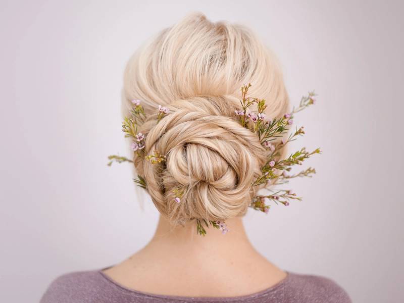 En person med lyst, oppsatt hår dekorert med små blomster og grener sett bakfra.