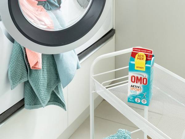 En vaskemaskin med klær og en trillekoffert med melkekartong på gulvet ved siden av.