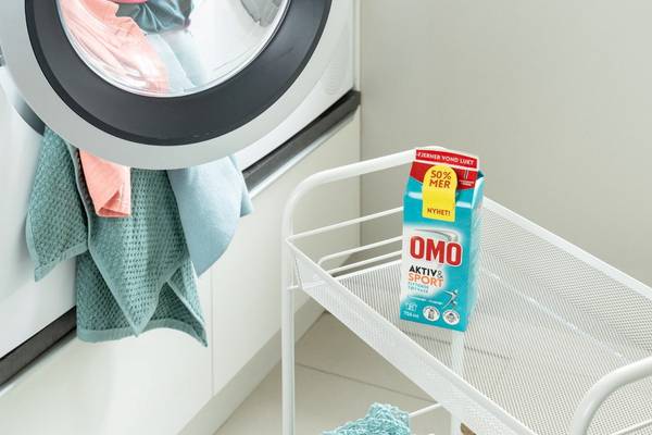 En vaskemaskin med klær og en trillekoffert med melkekartong på gulvet ved siden av.