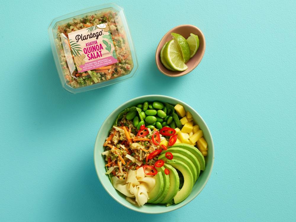 En asiatisk quinoasalat i en grønn bol med avokado, cherrytomater, edamamebønner og chili, med limebåter i en liten skål ved siden av.