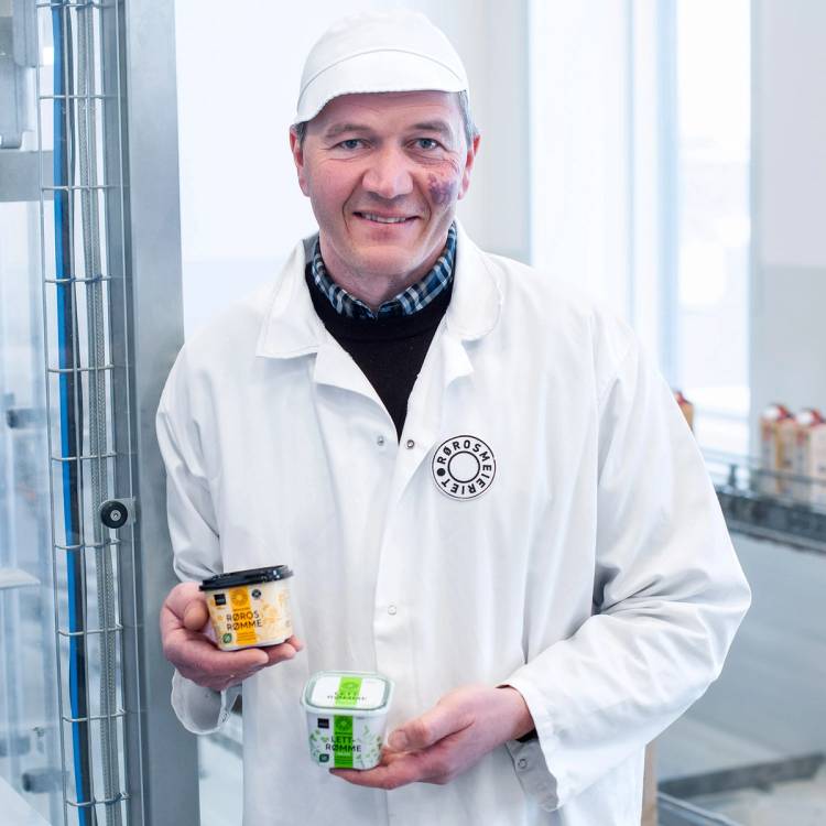 Person i hvit labfrakk holder to små beger med rømme på Røros Meieriet, lett rømme, i et produksjonsmiljø.