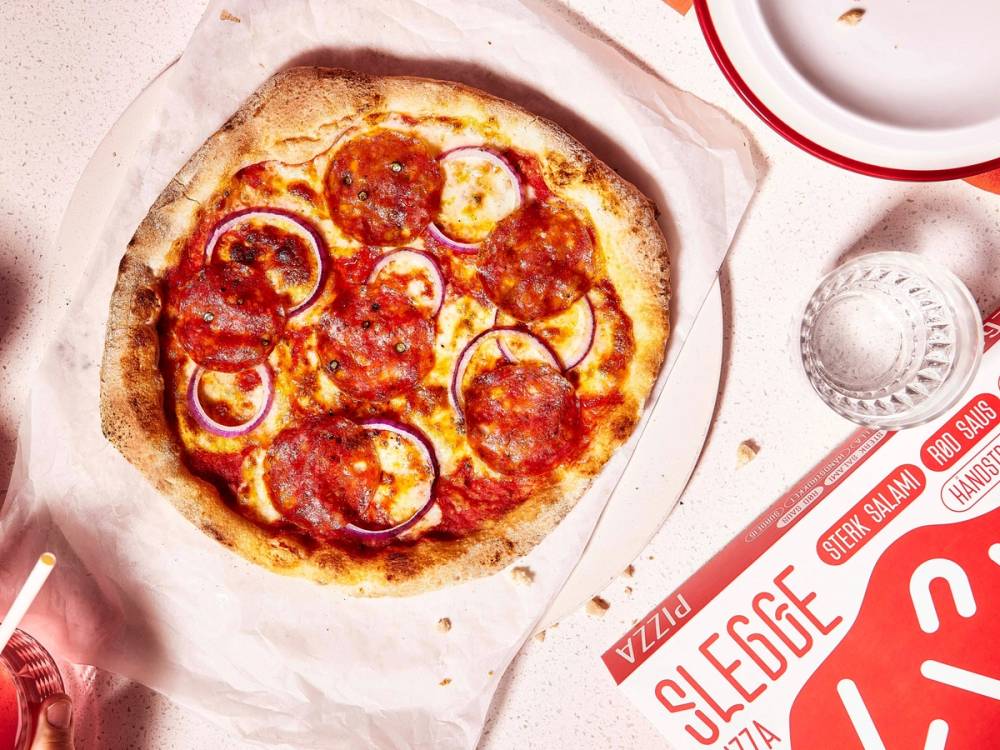 En pizza med pepperoni, løk og ost på en pizzabunn, ser ut til å være nybakt.