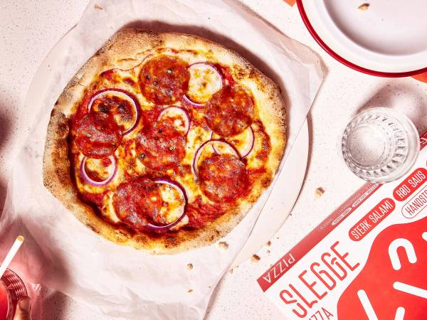 En pizza med pepperoni, løk og ost på en pizzabunn, ser ut til å være nybakt.