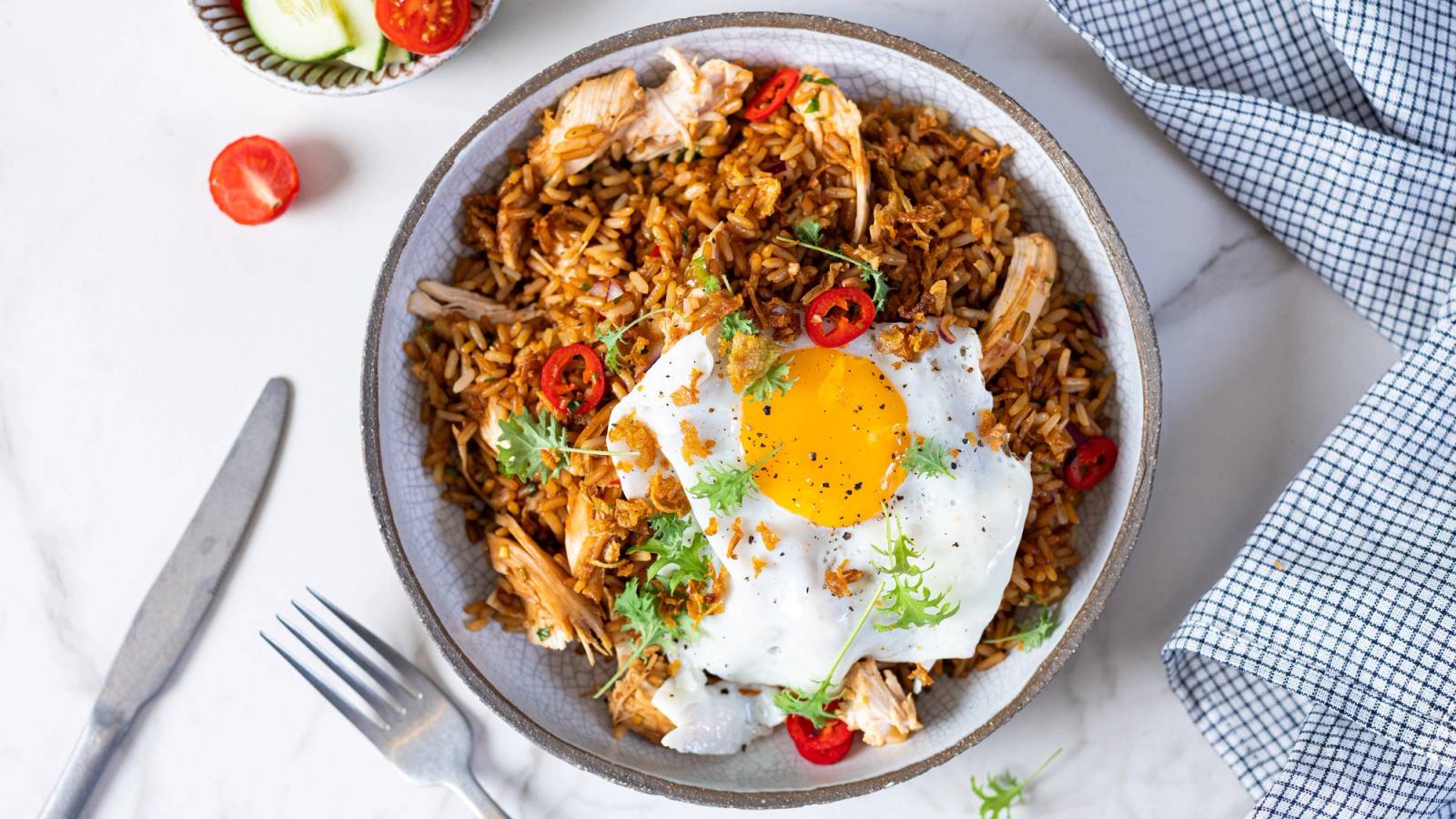 Ris med kylling, egg, grønnsaker og krydder på en tallerken, ser ut som nasigoreng.