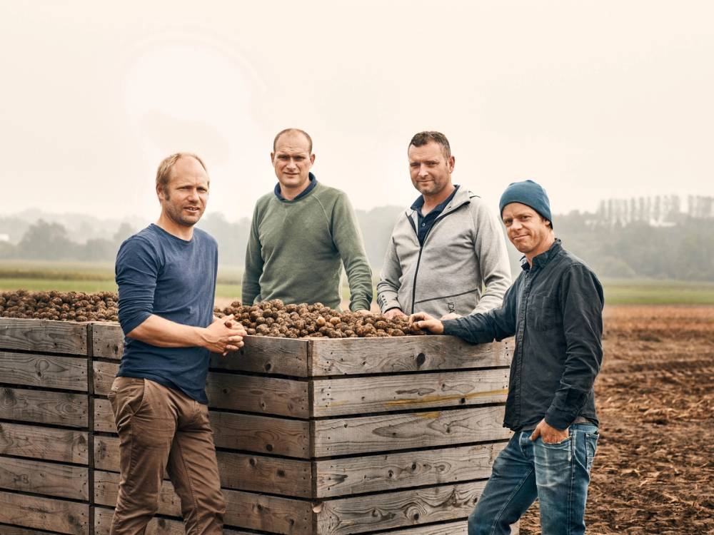 Fire personer står rundt en stor plantekasse fylt med jord, ute i et åpent landskap.
