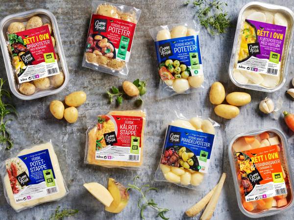 Pakker med ferdigkokte poteter og grønnsaker på is, med noen løk og urter rundt, på et kjøkkenbord.