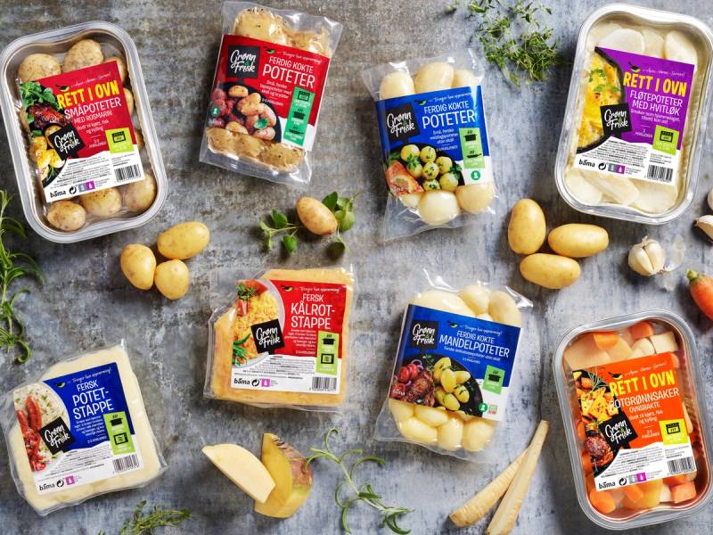 Pakker med ferdigkokte poteter og grønnsaker på is, med noen løk og urter rundt, på et kjøkkenbord.