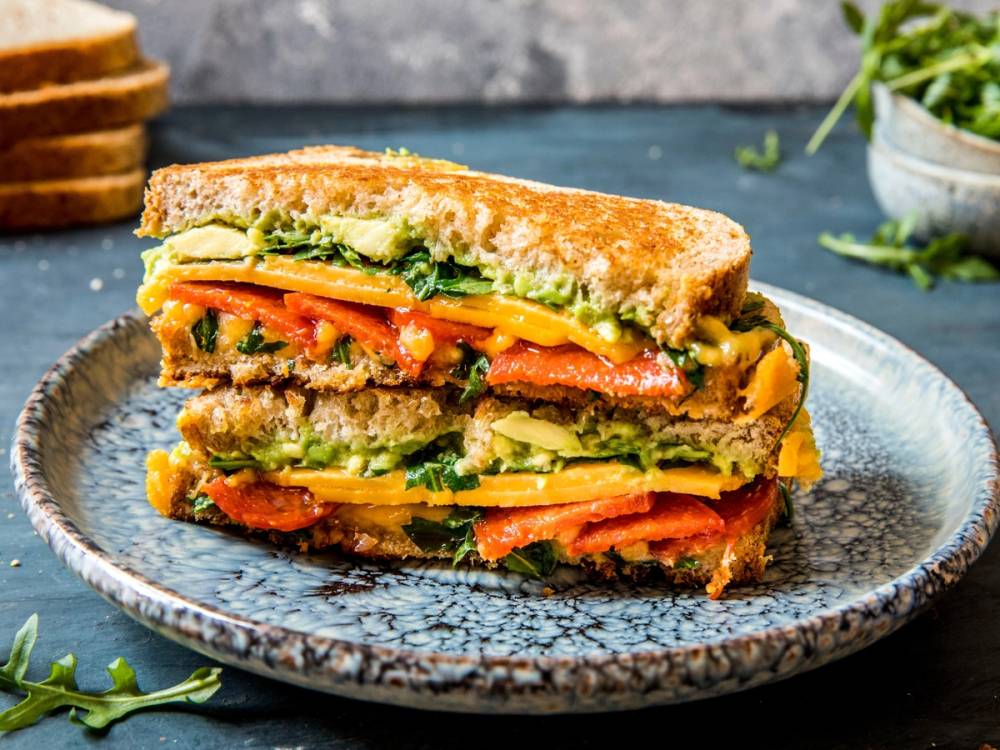 Fargerik og smakfull vegetarisk sandwich med grønnsaker og ost på en blå tallerken.