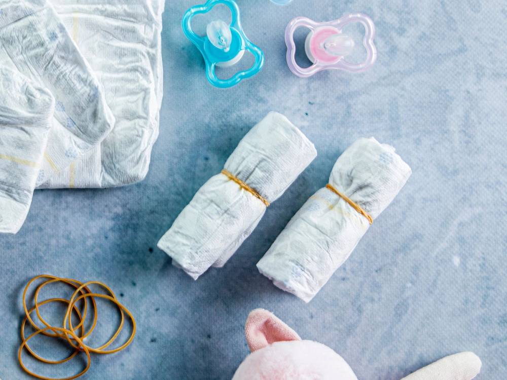 To bleier og to smokker ligger på en blå overflate, med en del andre babyrelaterte gjenstander rundt.