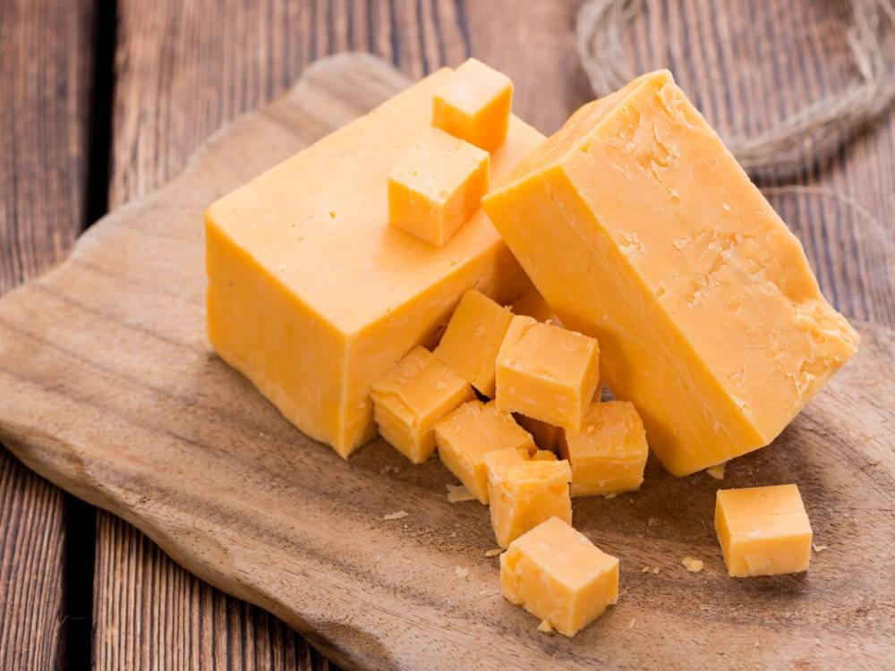 Ulike stykker med gul ost på et trebrett, klar til servering.