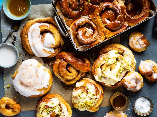 Kanelboller og andre bakverk på et fat med små kopper med sukker og sirup rundt.