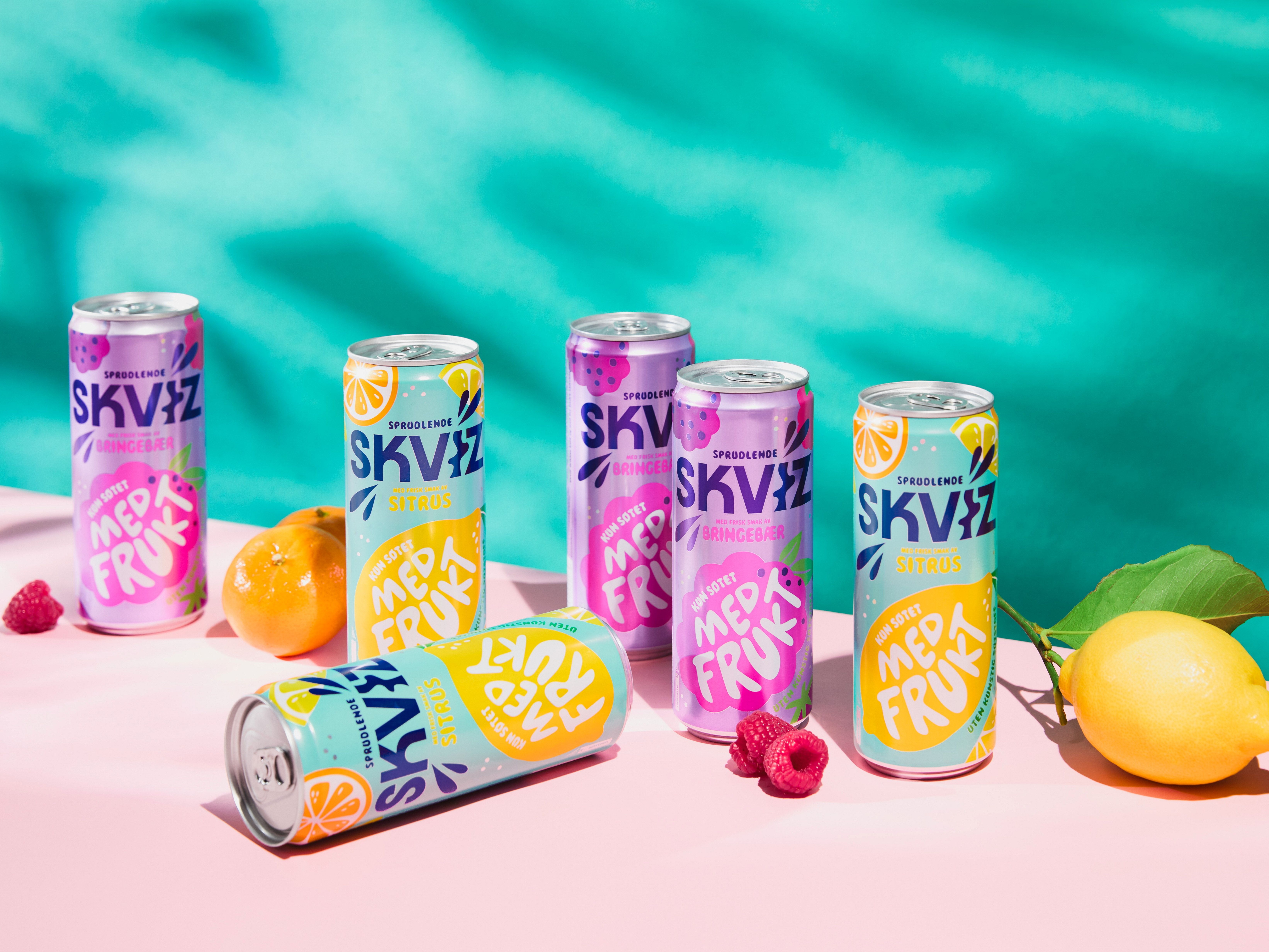 Flere bokser med SKVIZ frukt-smak på et bord med frukt rundt, mot en turkis bakgrunn.