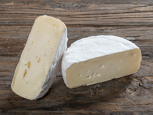 To stykker ost på en treplate, en med hvit skorpe og en uten, på et trebord.