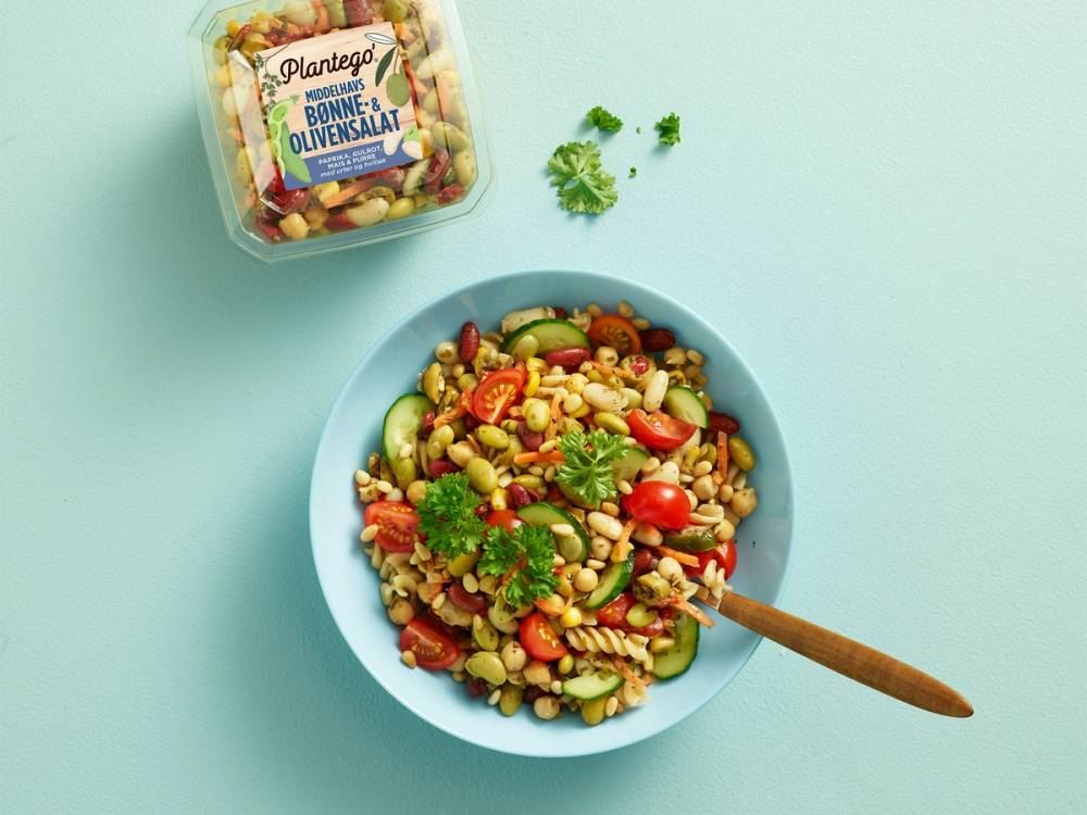 Bønnesalat med cherrytomater, kikerter og frisk koriander i en blå bolle, med en pakke plantego bønnesalat i bakgrunnen