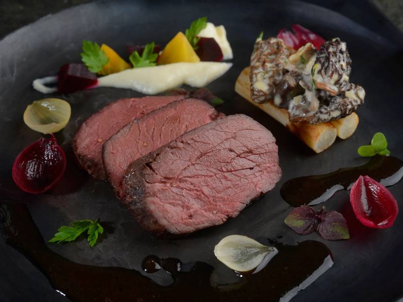 Et stykke rosa indrefilet av storfe servert med ulike grønnsaker og saus på en svart tallerken.