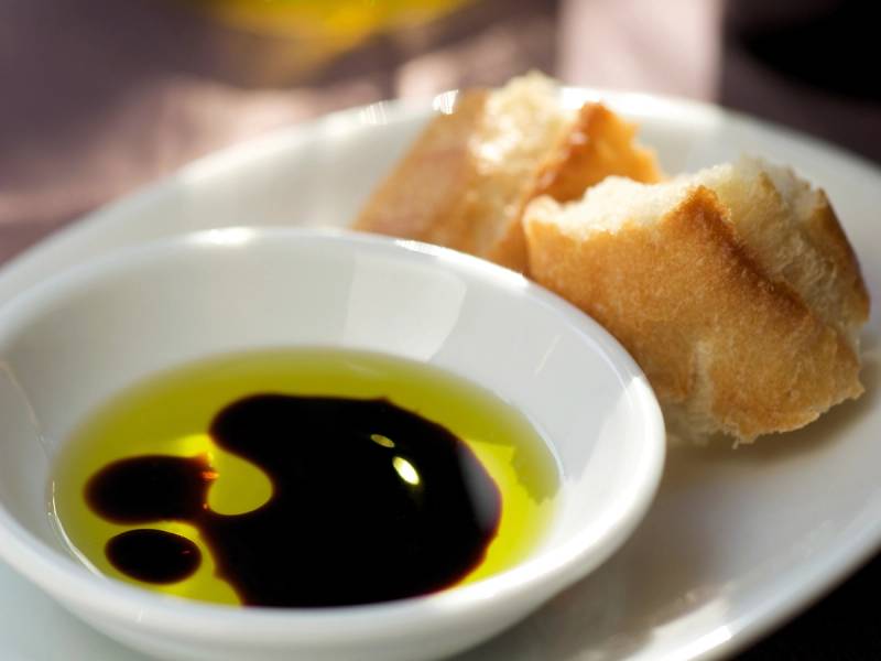 Olivenolje i en liten skål med brød på en tallerken ved siden av.