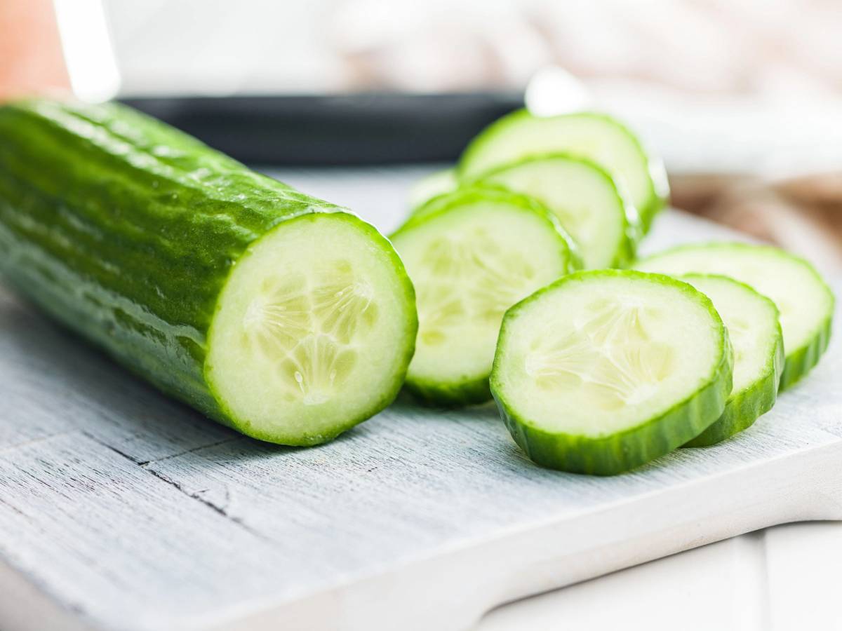Skivet agurk på en hvit skjæreflate med en hel agurk i bakgrunnen