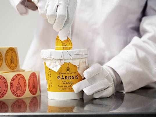 Person som pakker eller åpner en bøtte med Garddis iskrem, med flere små kanner ved siden av, på et lyst bord.