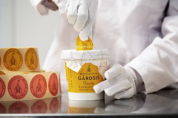 Person som pakker eller åpner en bøtte med Garddis iskrem, med flere små kanner ved siden av, på et lyst bord.