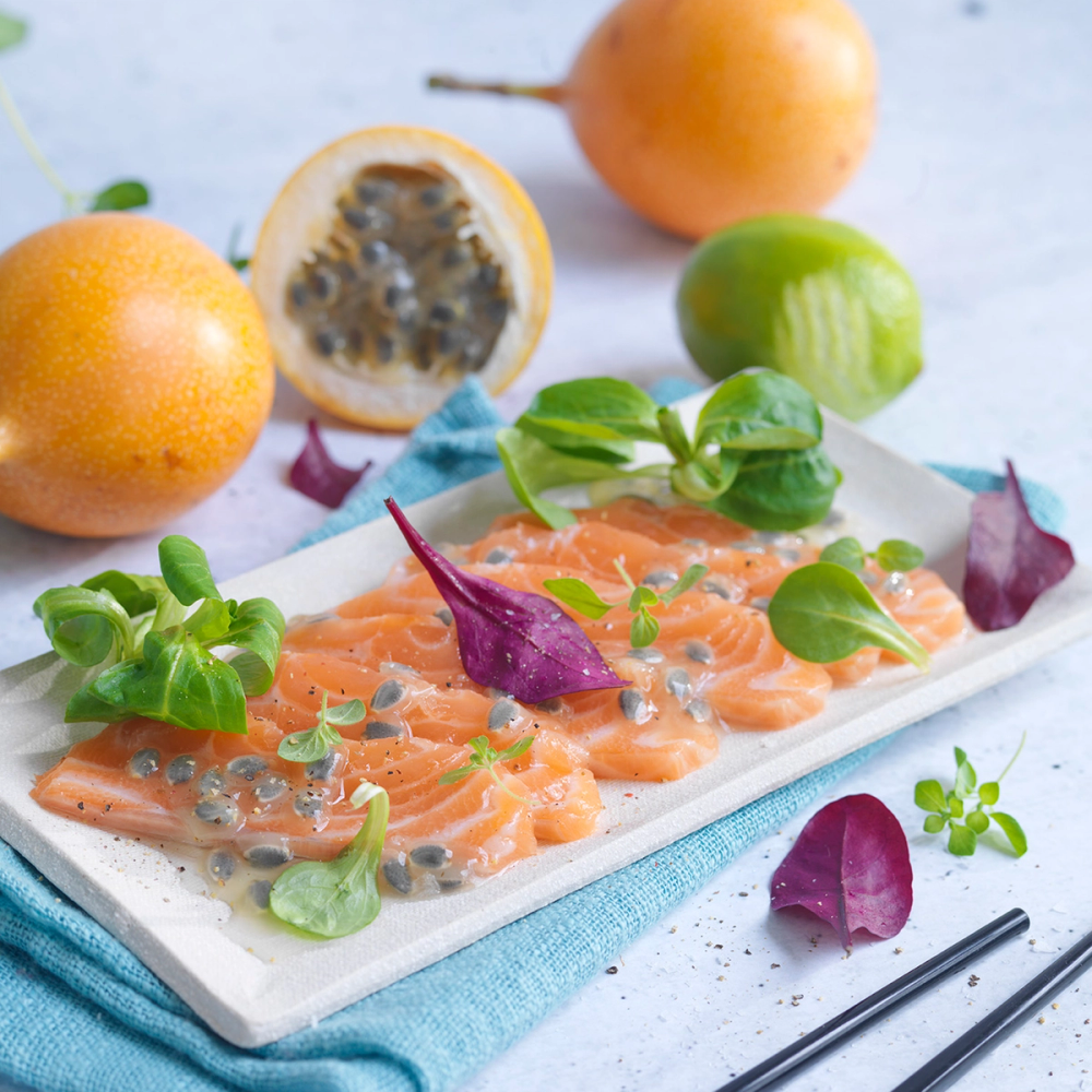 Laks med granatäppelkjerner og urter på en hvit tallerken, omgitt av frukt og grønnsaker