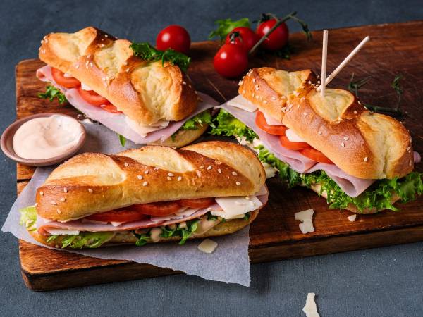 Tre pølser i pretzel pølsebrød med salat og tomater på et skjærebrett