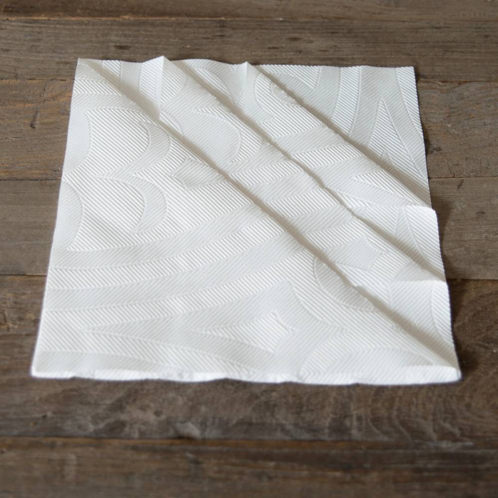 En hvit serviett med juledekorasjoner ligger brettet ut på et trebord.