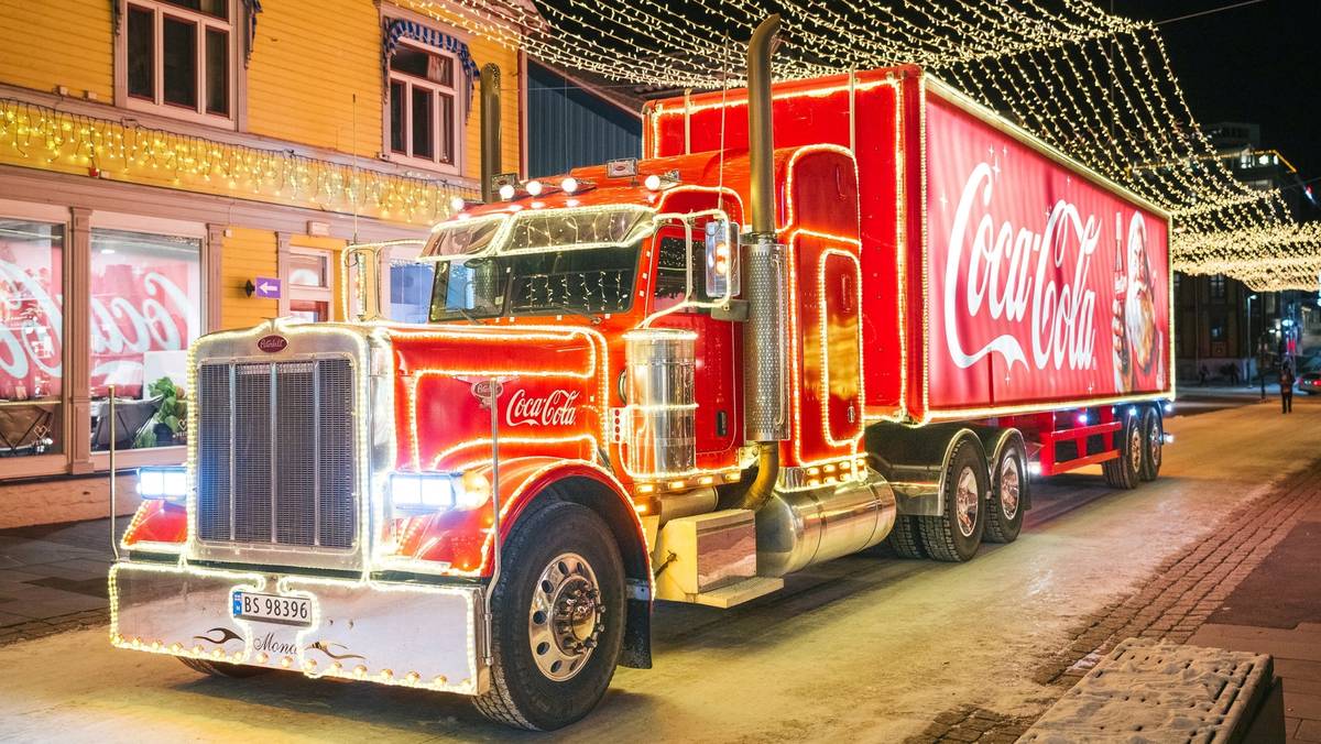 En stor Coca-Cola-lastebil parkert på en gate pyntet med julelys om kvelden.