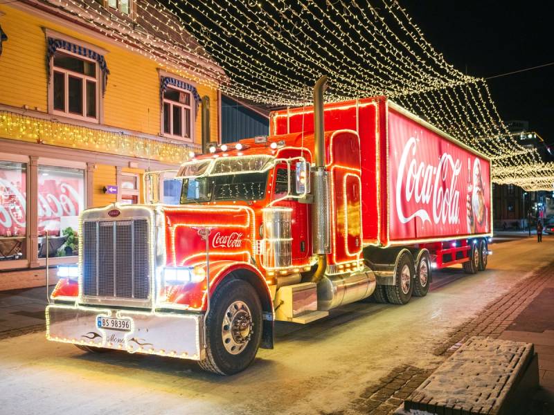 En stor Coca-Cola-lastebil parkert på en gate pyntet med julelys om kvelden.