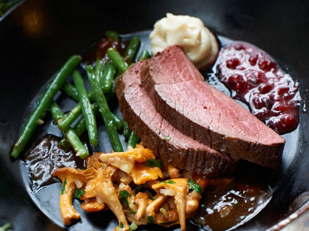 Ovnsbakt reinsdyrplomme med grønne bønner, potetmos og tyttebærsyltetøy på en tallerken