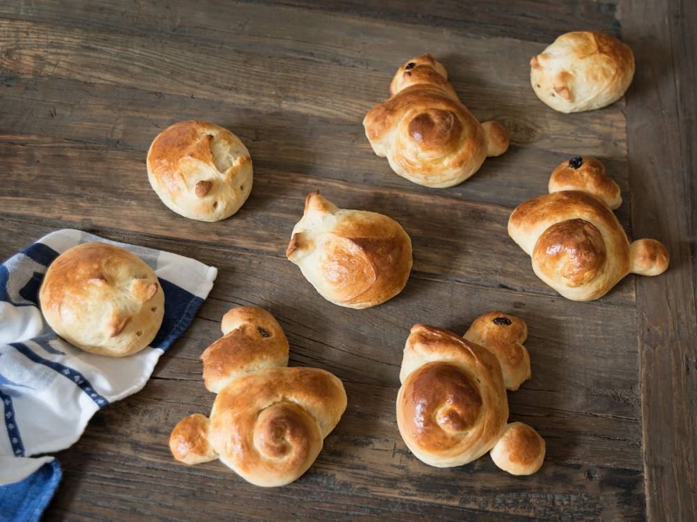 Ferske påskeboller på et trebord, noen ligger på en blå og hvit klut, og flere er plassert rundt.