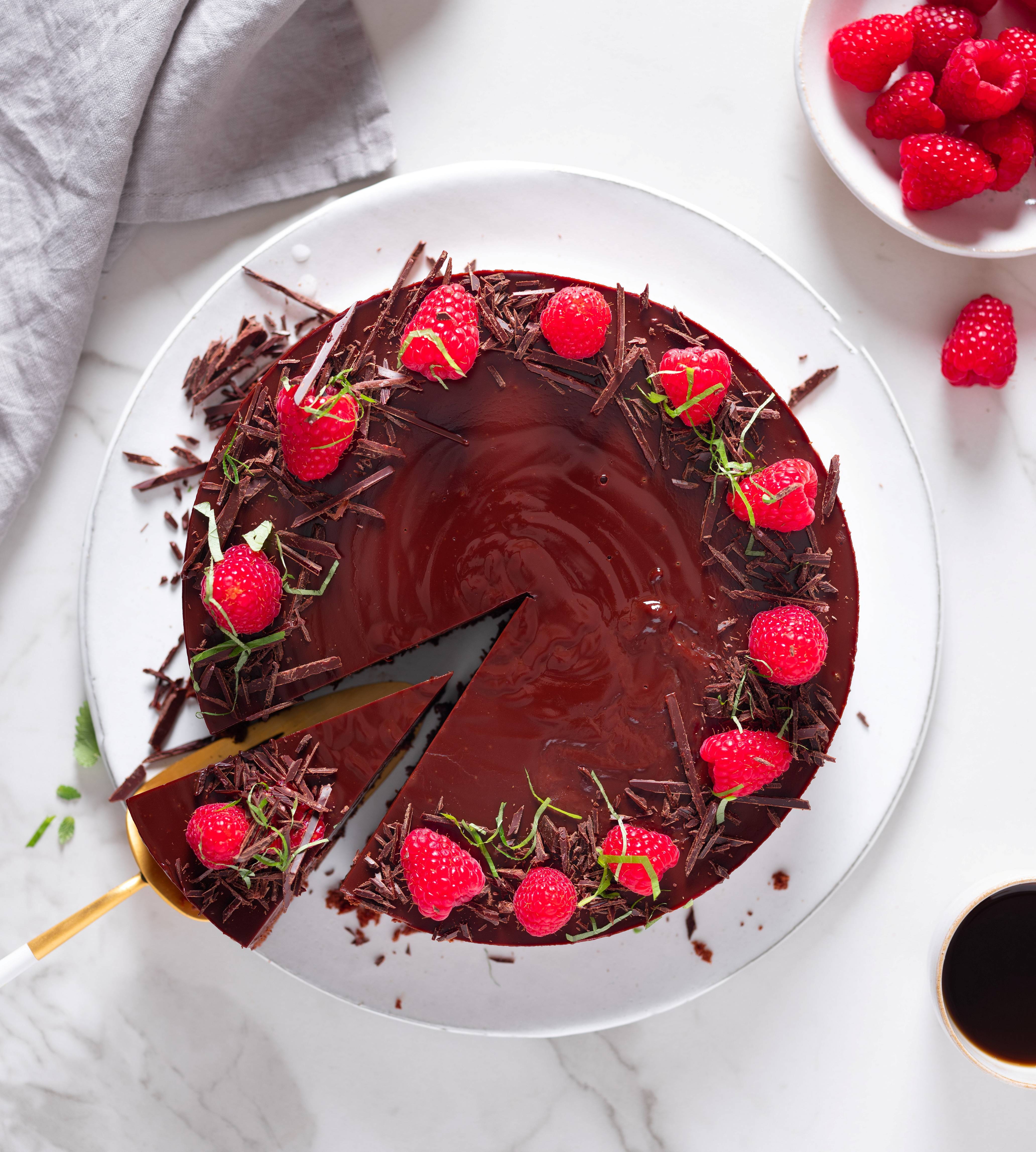 Sjokoladekake pyntet med friske bringebær og sjokoladestykker på en hvit tallerken