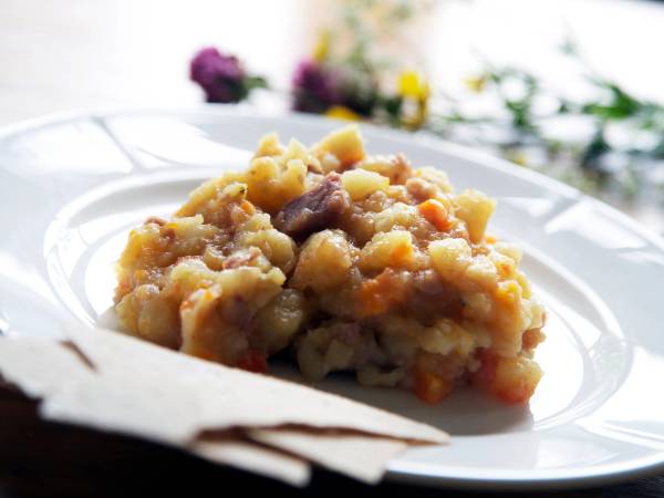 En porsjon med lapskaus på en hvit tallerken med blomster i bakgrunnen.