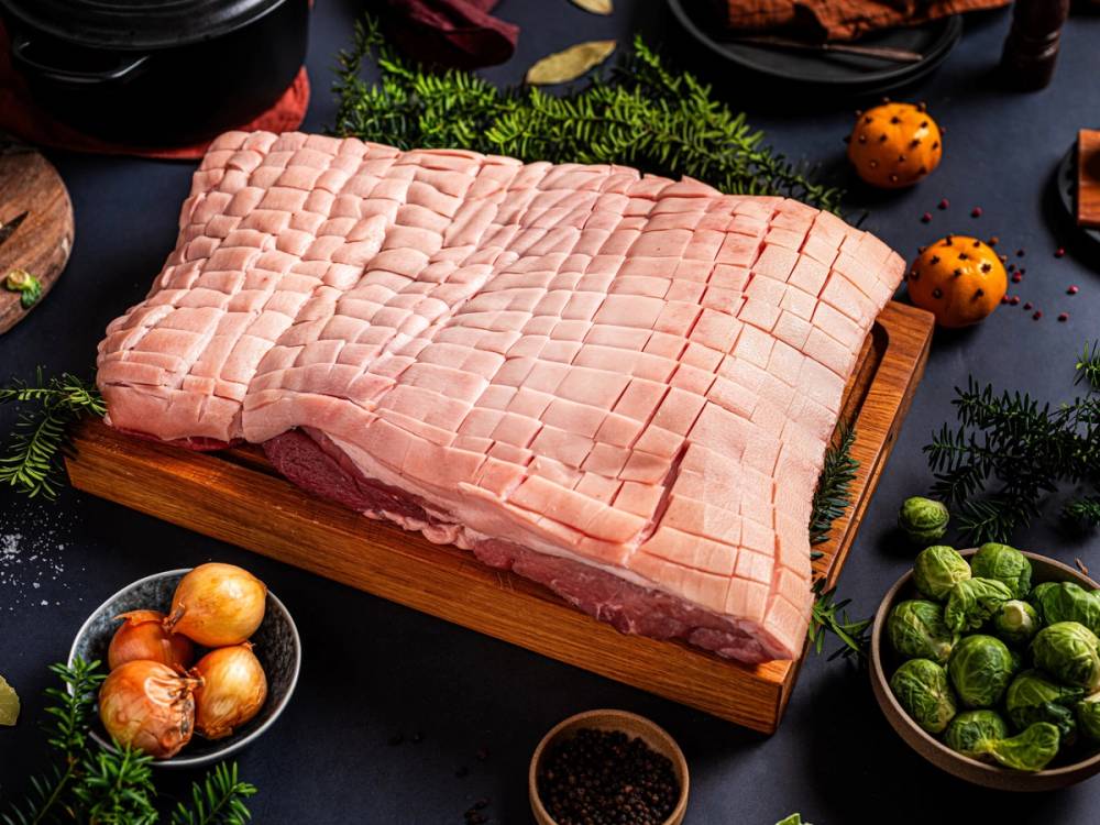 Ribbe med snittmønster ligger på skjærebrett, omgitt av grønnsaker og krydder på et mørkt bord.