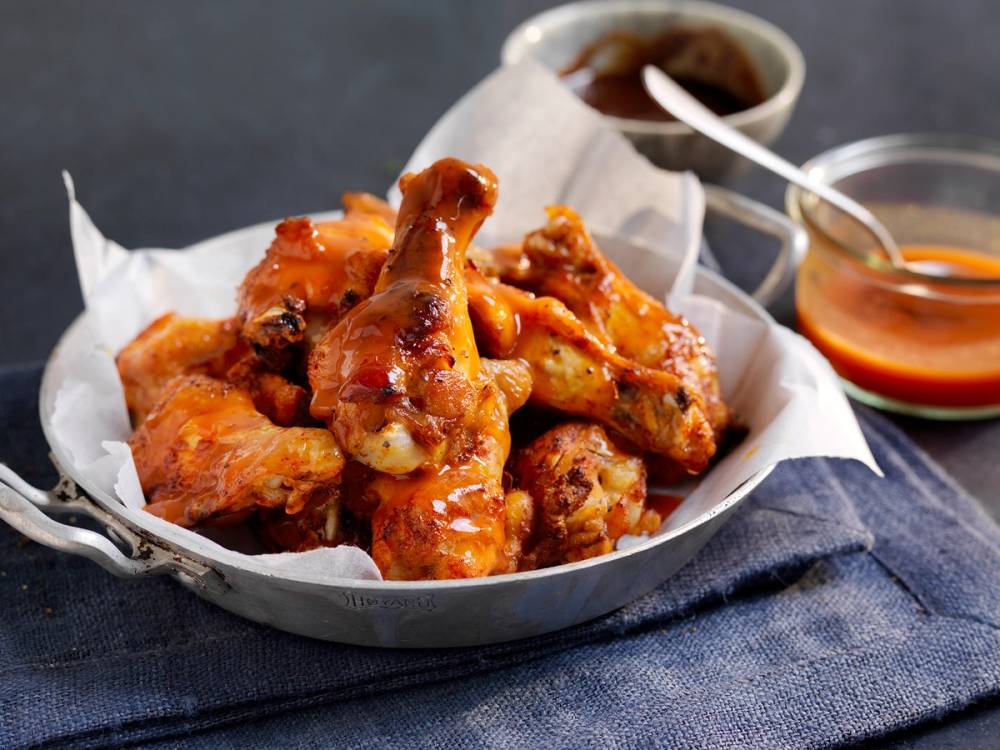Buffalowings ser ut til å være sprø og dekket av en rødlig saus, med en liten skål med saus ved siden av.