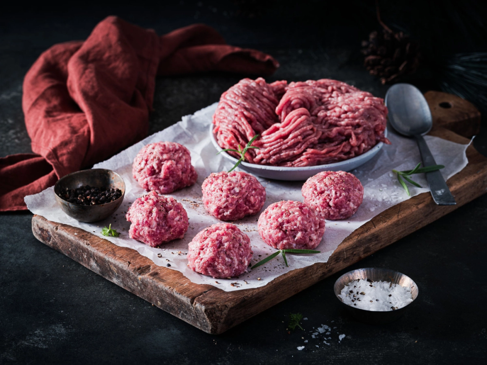 Medisterkaker på et skjærebrett med en skje og krydderurter, klar til å bli stekt eller servert.