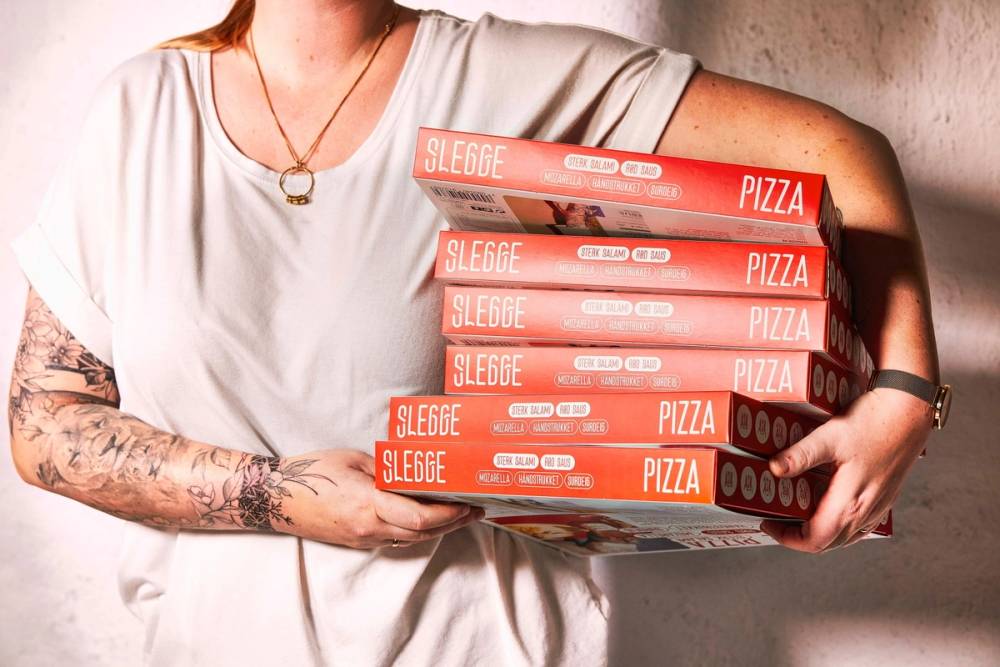 En person holder flere pizzaesker med Slege logo og teksten 'Pizza' på, mot en lys bakgrunn.
