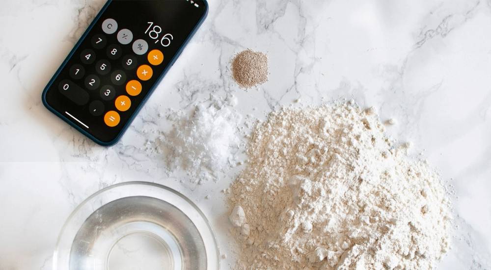 En kalkulator med tall og en bolle med mel på et kjøkkenbord, brukt til pizzadeig.