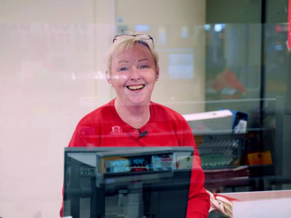 En person i rødt arbeidstøy står bak kassen i en butikk, med en skjerm foran seg.