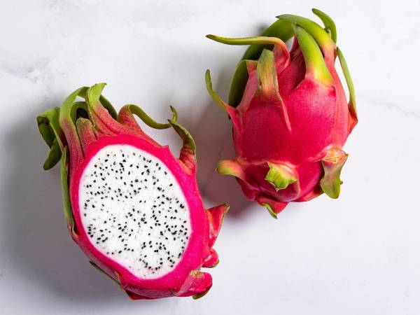 En hel og en halvert pitahaya (dragefrukt) med rosa skinn og hvitt kjøtt med svarte frø, plassert på en lys bakgrunn.