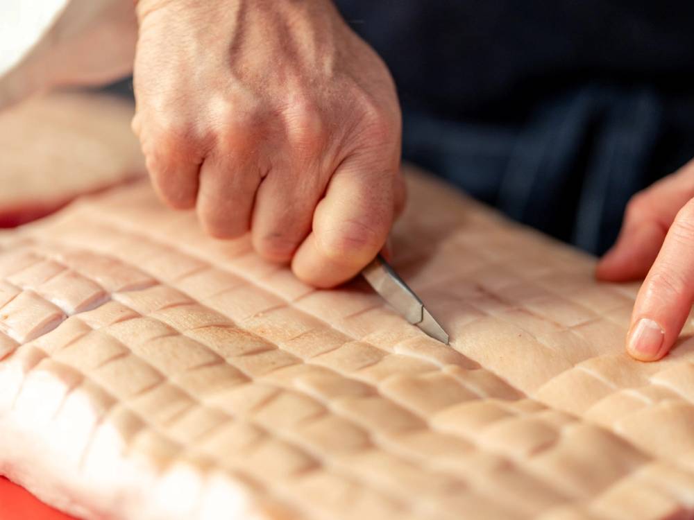 En person skjærer i tarmene på en stor kjøttbit med en kniv.