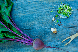 Rødbete med grønne blader ligger på en blå treflate, med noen små deler og en gaffel i nærheten.