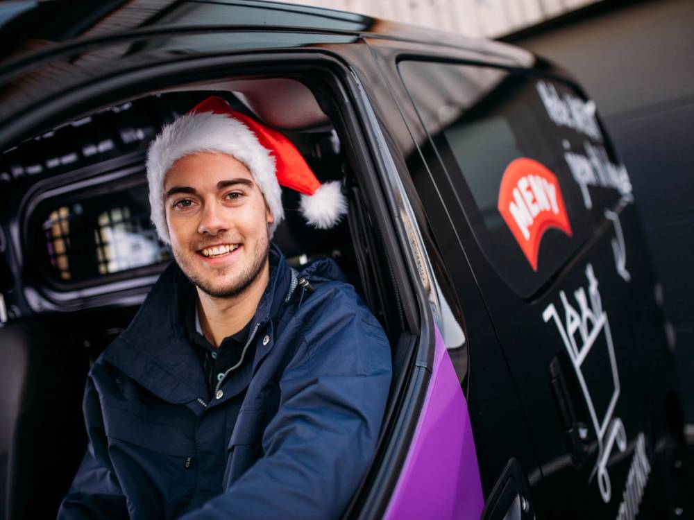 Nettbutikk sjåfør med nisselue som sitter i førersetet av en bil med logo på døren.