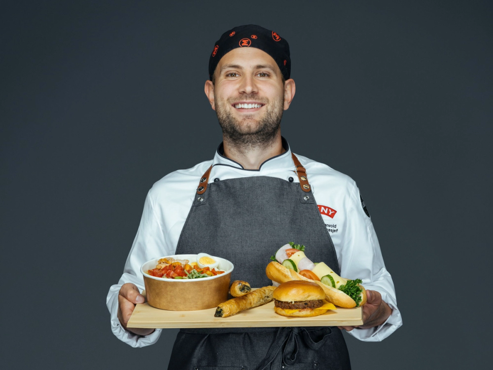 Person i kokkeantrekk holder brett med salat, baguette, angusburger og børek