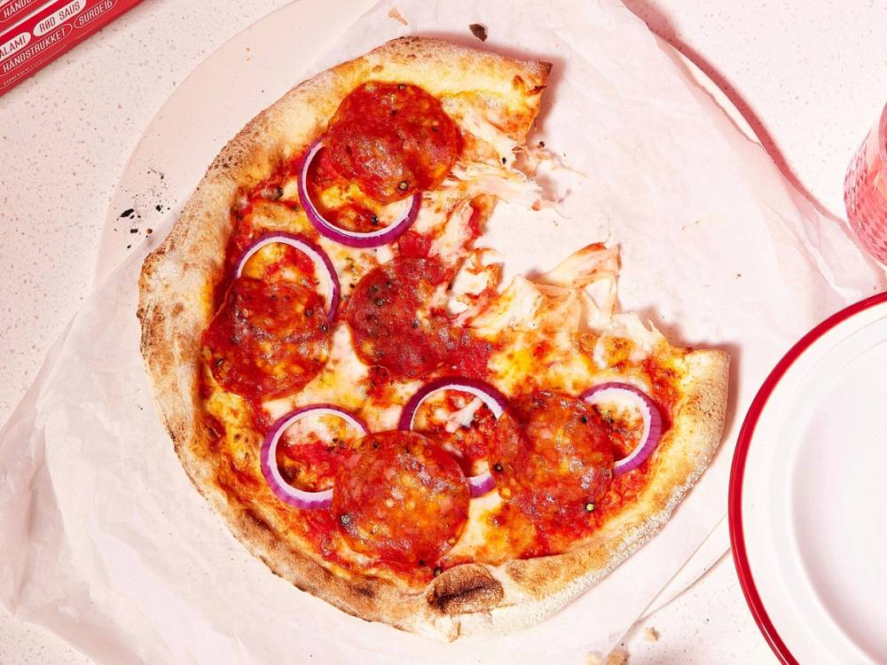 En pizza med pepperoni og løk, delvis spist, på et hvitt fat.