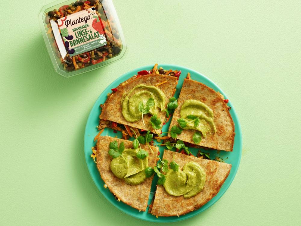 Mexicansk bønnesalat servert på en tallerken med avokadobiter og en liten pakke med salat ved siden av, på en grønn bakgrunn.